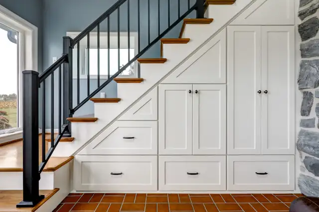 Staircase with black balusters and built-in white storage cabinets underneath